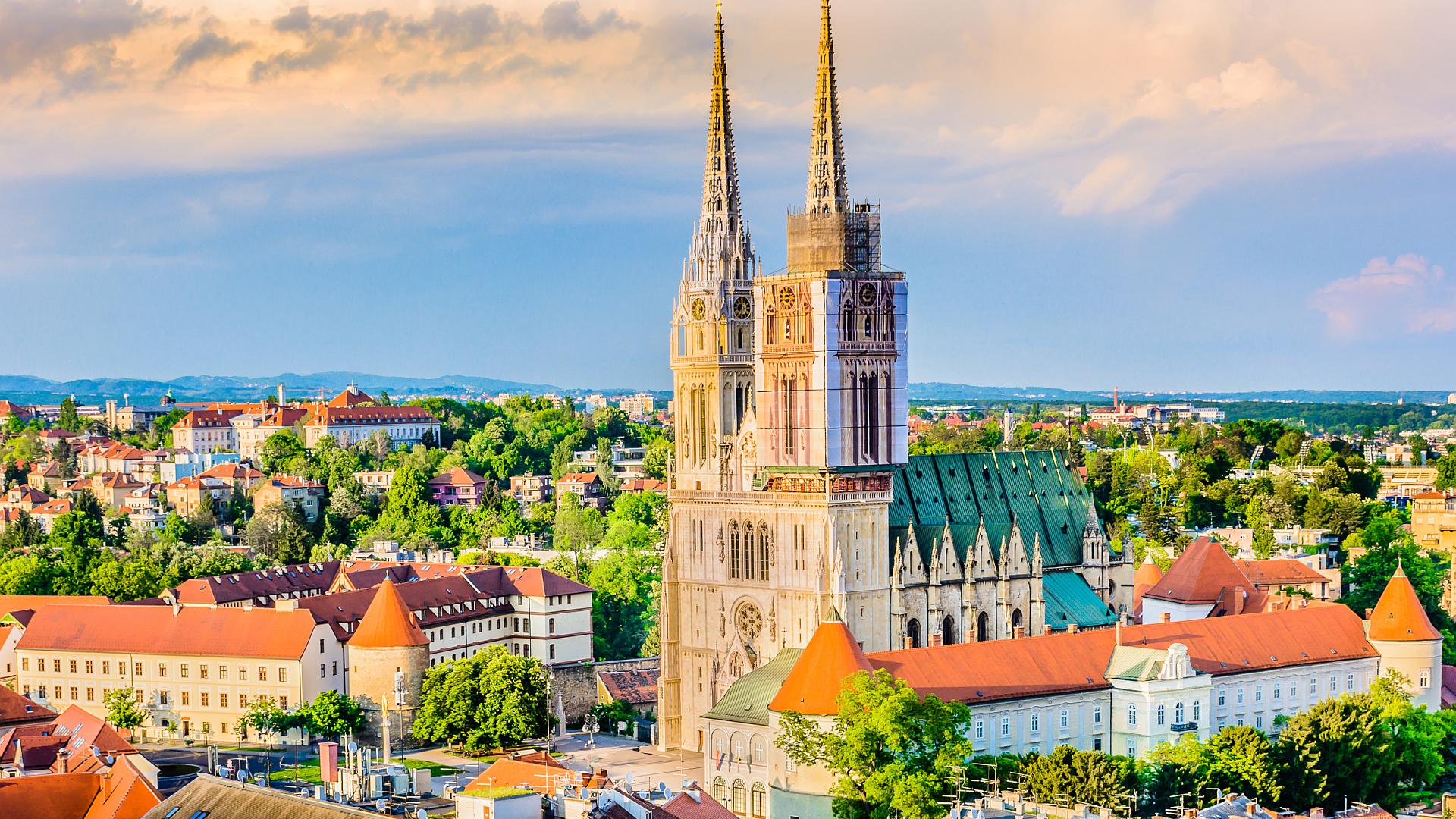 The imposing neo-Gothic spires of Zagreb Cathedral soaring into the sky, with construction netting visible on one spire.